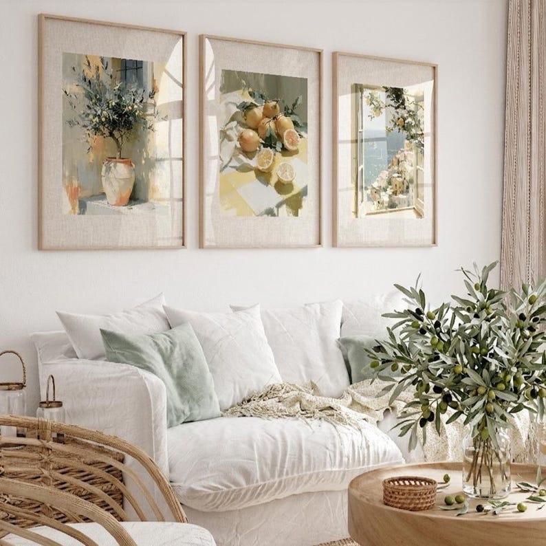 May include: Three framed watercolor prints depicting botanical and coastal scenes. The prints feature a vase with a plant, lemons on a table, and a coastal view through a window. The frames are light-colored wood, and the overall aesthetic is bright and airy.