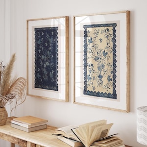 May include: Two rectangular framed wall art prints featuring intricate blue and white botanical and bird illustrations. The left print has a dark blue background, while the right print has a light cream background, both enclosed in light wood frames.