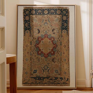 May include: Framed vintage rug art. The rug features a central medallion in red, blue, and gold hues, surrounded by intricate floral patterns. The border is a deep blue with floral motifs. The artwork is displayed in a gold frame.