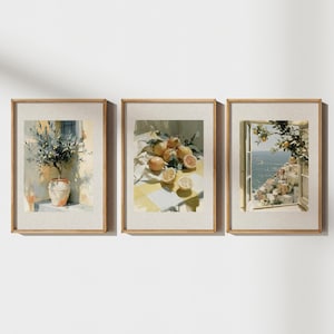 May include: Set of three framed art prints. The prints feature watercolor paintings of lemons, an olive tree in a pot, and a coastal view from a window. The frames are a light wood color, and the art has a soft, warm color palette.