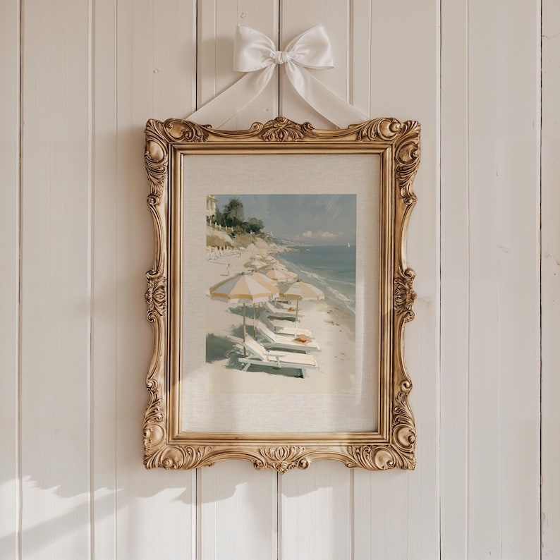 Amalfi beach with striped yellow umbrellas and white sun loungers art print displayed in a large ornate antique gold vintage frame hanging on a white shiplap panelled wall, suspended with a white satin ribbon bow — coastal Italian oil painting print with printed linen mat background