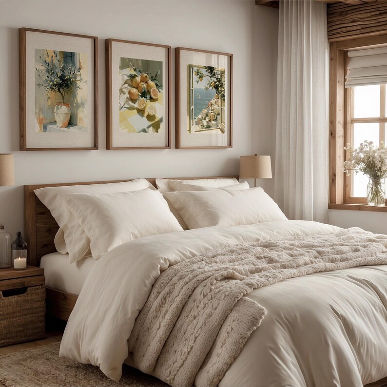 May include: A bedroom scene featuring a wooden bed frame with white bedding and a beige cable-knit throw blanket. Above the bed are three framed watercolor prints with botanical and coastal themes. A nightstand and window are visible.