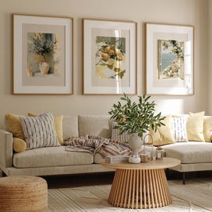 May include: Three framed art prints with botanical themes hang above a beige sofa with yellow and striped pillows. A wooden coffee table with a slatted base sits on a patterned rug. A vase of greenery is on the table.