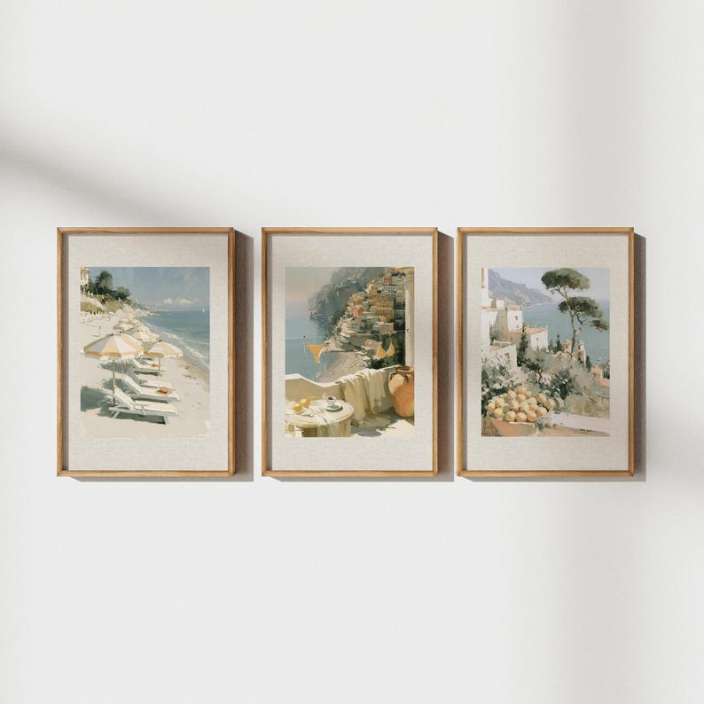 All three Amalfi Coast Italian triptych prints mounted on a pure white wall in matching antique gold oak frames — left print shows Amalfi beach with yellow striped umbrellas, center shows Positano balcony with terracotta jug and sea view, right shows Amalfi lemon terrace with umbrella pine and white architecture