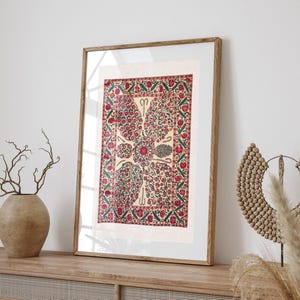 May include: A framed rectangular print featuring a cream-colored background with a central floral motif. The design includes intricate red and green botanical patterns arranged in a symmetrical layout, enclosed by a decorative red and green border.