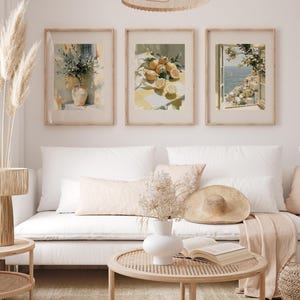 May include: Three framed art prints featuring watercolor paintings. One depicts a vase of flowers, another lemons on a table, and the third a coastal view. The prints are displayed above a white sofa.