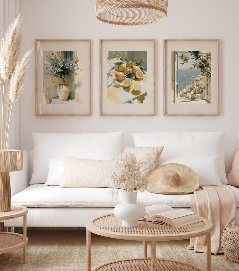 May include: Three framed art prints featuring watercolor paintings. One depicts a vase of flowers, another lemons on a table, and the third a coastal view. The prints are displayed above a white sofa.