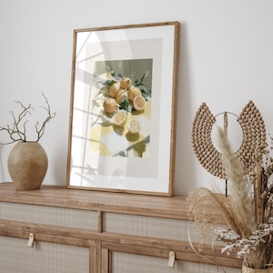 May include: A framed art print featuring a still life of lemons. The painting depicts whole and sliced lemons on a yellow and white checkered surface, with green leaves. The frame is a light brown color.