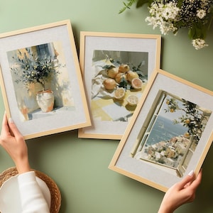 May include: Three framed art prints with light wood frames. The prints depict scenes of lemons, olive trees, and a coastal town. The art has a soft, painterly style with a neutral linen matting.