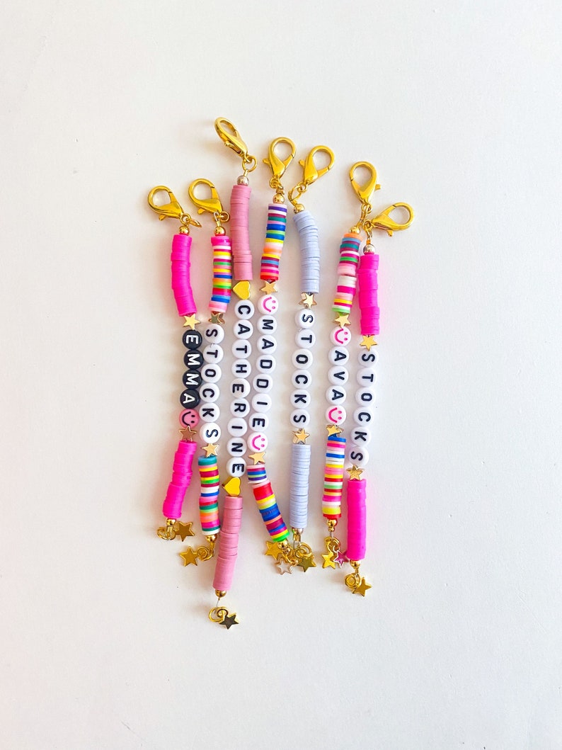 Puede incluir: Un conjunto de seis pulseras de cuentas coloridas con abalorios de estrellas doradas y nombres personalizados, incluyendo "Emma", "Stocks", "Catherine", "Maddie", "Sava" y "Stocks".