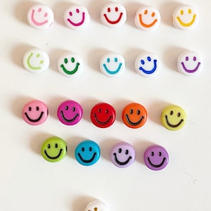 Puede incluir: Surtido de cuentas de caritas sonrientes de colores con contornos negros. Las cuentas son de pl&aacute;stico y vienen en una variedad de colores, incluyendo amarillo, naranja, rojo, rosa, morado, azul, verde y blanco.