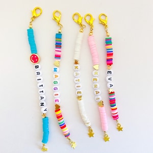 Puede incluir: Cinco pulseras de cuentas coloridas con cierres y dijes dorados. Cada pulsera tiene un nombre diferente escrito en cuentas blancas: Brittany, Maggie, Katie, Kenai y Eva. Los dijes son una carita sonriente, un coraz&oacute;n, una estrella, un coraz&oacute;n y una estrella.