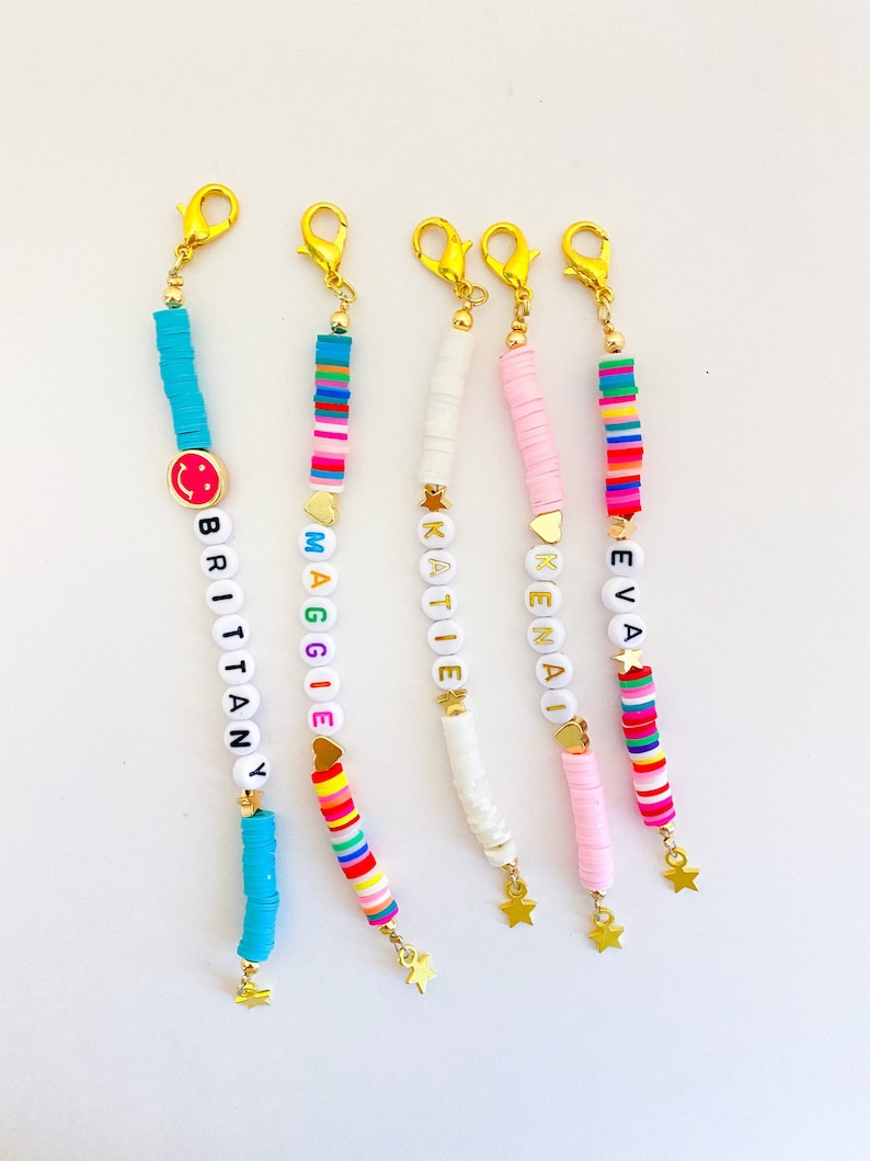 Puede incluir: Cinco pulseras de cuentas coloridas con cierres y dijes dorados. Cada pulsera tiene un nombre diferente escrito en cuentas blancas: Brittany, Maggie, Katie, Kenai y Eva. Los dijes son una carita sonriente, un coraz&oacute;n, una estrella, un coraz&oacute;n y una estrella.