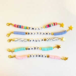 Puede incluir: Cinco pulseras de cuentas coloridas con abalorios de estrellas doradas y cuentas de letras blancas que deletrean los nombres "Emily", "Brittany", "Paula", "Madz" y "Sydney".