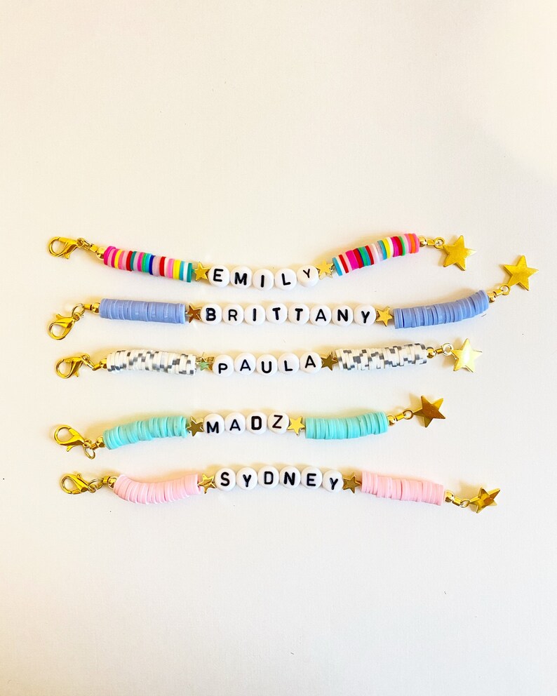 Puede incluir: Cinco pulseras de cuentas coloridas con abalorios de estrellas doradas y cuentas de letras blancas que deletrean los nombres "Emily", "Brittany", "Paula", "Madz" y "Sydney".
