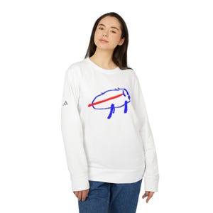 Può includere: Felpa bianca con grafica di un bufalo blu e rosso. La felpa girocollo ha maniche lunghe. Il logo Adidas è sulla manica sinistra.