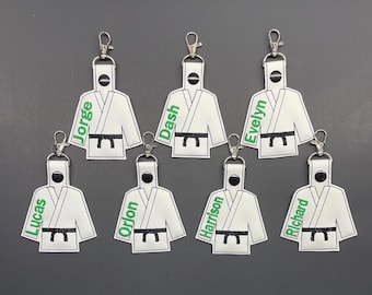 May include: Seven white karate uniform keychains with black belts and green embroidered names: Lucas, Jorge, Dash, Evelyn, Orlon, Harrison, and Richard.