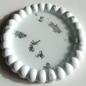 May include: A round, white decorative tray with a beaded edge. The interior of the tray is a pale blue with silver leaf accents scattered throughout. The tray is a decorative item.