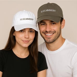 Może przedstawiać: Dwie osoby w czapkach bejsbolowych z haftowanym tekstem "XII.XX.MMMXIV" z przodu. Kobieta ma na sobie białą czapkę i czarną koszulkę. Mężczyzna ma na sobie zieloną czapkę i białą koszulkę.