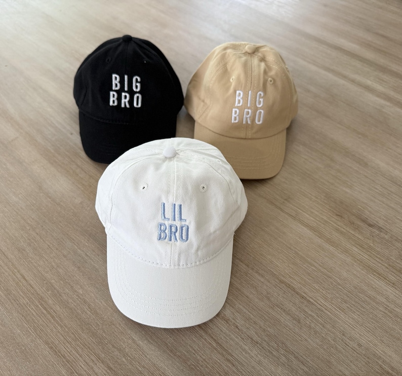 Puede incluir: Tres gorras de b&eacute;isbol en negro, beige y blanco. Las gorras negras y beige tienen "BIG BRO" bordado en blanco, mientras que la gorra blanca tiene "LIL BRO" bordado en azul. Las gorras est&aacute;n hechas de tela suave.