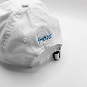 Puede incluir: Gorra de b&eacute;isbol blanca con el nombre "Peter" bordado en hilo azul en el lateral. La gorra tiene una visera curva y una correa ajustable en la parte trasera. Fabricada en tejido suave y texturizado.