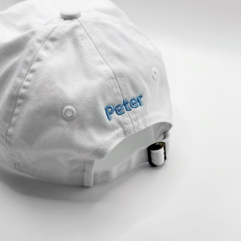 Puede incluir: Gorra de b&eacute;isbol blanca con el nombre "Peter" bordado en hilo azul en el lateral. La gorra tiene una visera curva y una correa ajustable en la parte trasera. Fabricada en tejido suave y texturizado.