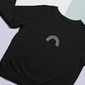 Op de afbeelding: Zwart sweatshirt met een wit regenboogontwerp op de voorkant.
