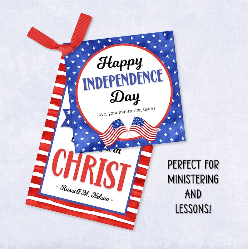 May include: Two rectangular paper tags with red ribbon. The top tag features a blue background with white stars, two American flags, and the text Happy Independence Day love, your ministering sisters. The bottom tag has red stripes and text CHRIST.