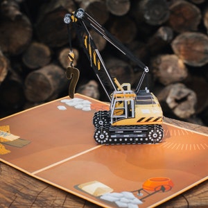 May include: A yellow and black construction crane pop-up card. The crane is lifting a question mark. The card is open and shows a brown background with a construction scene.