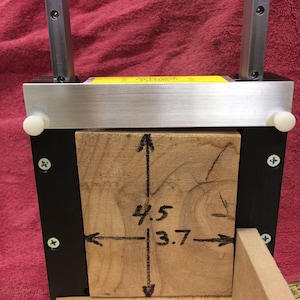 May include: A wooden block is clamped in a metal frame. The block is marked with measurements of 4.5 inches by 3.7 inches.