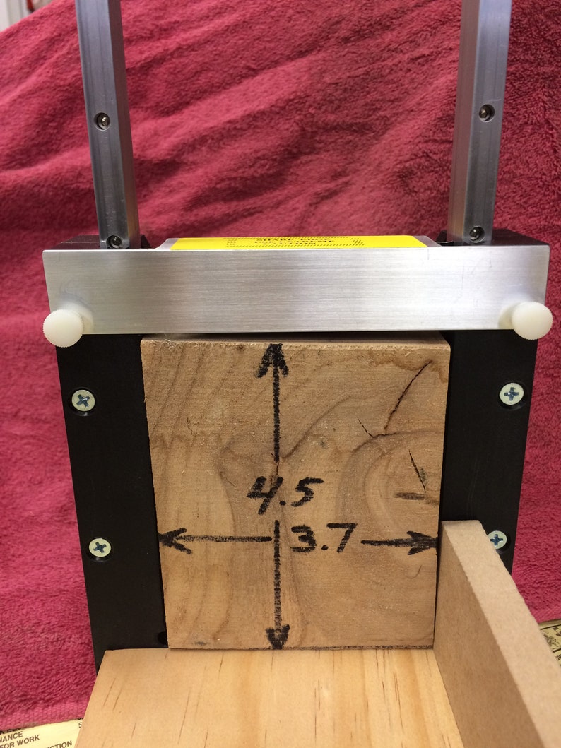 May include: A wooden block is clamped in a metal frame. The block is marked with measurements of 4.5 inches by 3.7 inches.