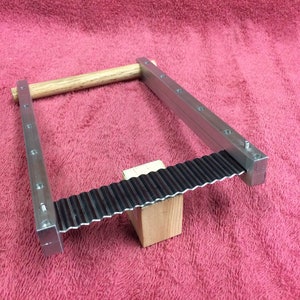 K&ouml;nnte beinhalten: Ein Metall-Crimpzange mit einem Holzgriff. Die Zange ist aus silbernem Metall und hat eine schwarze Metall-Crimpfl&auml;che. Die Zange liegt auf einer rosa Oberfl&auml;che.