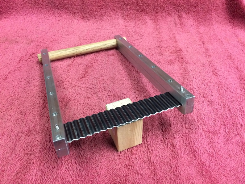 K&ouml;nnte beinhalten: Ein Metall-Crimpzange mit einem Holzgriff. Die Zange ist aus silbernem Metall und hat eine schwarze Metall-Crimpfl&auml;che. Die Zange liegt auf einer rosa Oberfl&auml;che.