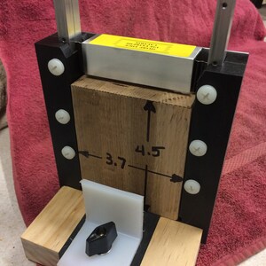 K&ouml;nnte beinhalten: Ein Holzblock mit einer Metallstange oben. Der Block ist mit den Ma&szlig;en 3,7 Zoll und 4,5 Zoll gekennzeichnet. Der Block ist mit Schrauben an einem schwarzen Rahmen befestigt.