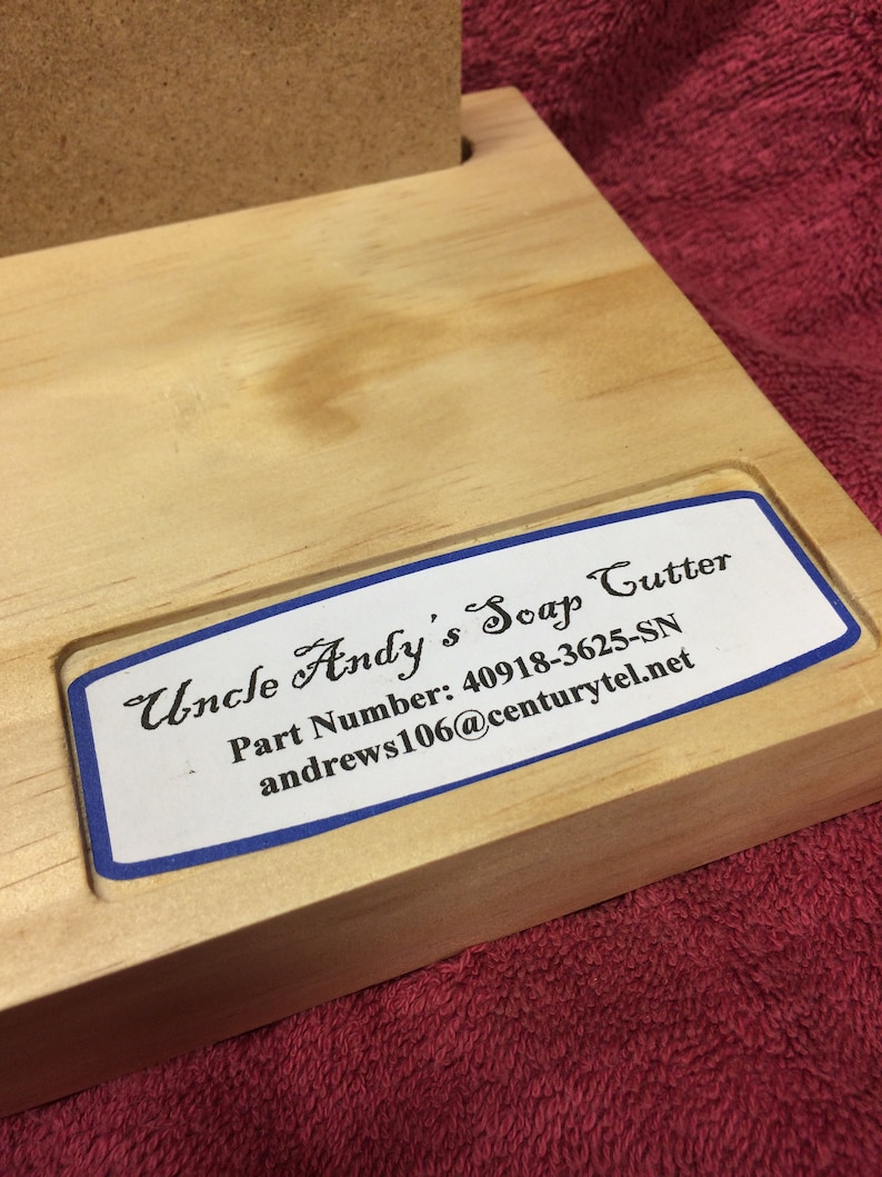 K&ouml;nnte beinhalten: Ein h&ouml;lzerner Seifen-Schneider mit einem blauen und wei&szlig;en Etikett, auf dem "Uncle Andy's Soap Cutter", "Part Number: 40918-3625-SN" und "andrews106@centurytel.net" steht.