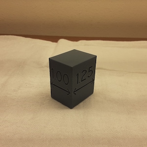 May include: A gray cube with the measurements 1.00 inches and 1.25 inches marked on it.