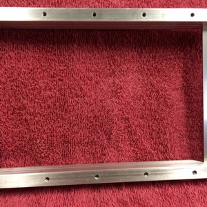 May include: A silver metal frame with a wooden handle. The frame has multiple holes along the top and bottom edges.