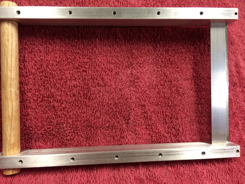 May include: A silver metal frame with a wooden handle. The frame has multiple holes along the top and bottom edges.