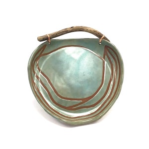 May include: A teal ceramic bowl with a natural wood handle and brown lines. The bowl is glazed and has a slight sheen.