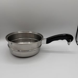 May include: Stainless steel saucepan with a black handle. The pan has a round shape and a handle with a loop at the end. The pan is designed for cooking and is made of a shiny, silver-colored metal.
