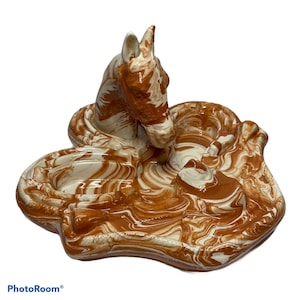 May include: A ceramic ashtray with a horse design. The ashtray is brown and white with a swirled pattern. It has three separate compartments for cigarettes.