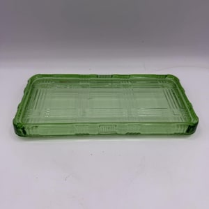 May include: A rectangular, light green glass tray with a plaid pattern etched into the surface. The tray has a raised, decorative border. The glass is translucent, and the tray is empty.