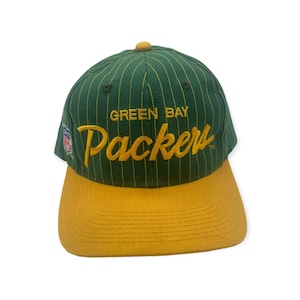 May include: Green Bay Packers baseball cap with a green and yellow striped crown and a yellow brim. The cap has the team's logo and the words "Green Bay Packers" embroidered on the front.