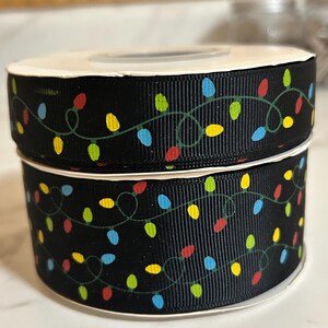 May include: Two spools of black ribbon with a white string lights pattern. The lights are red, yellow, blue, and green.