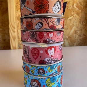 May include: A stack of five colorful ribbon spools with a horror movie theme. The ribbons feature various characters and designs, including a clown, a man with a knife, and flowers. The text "We All Float Down Here" is visible on one of the ribbons.