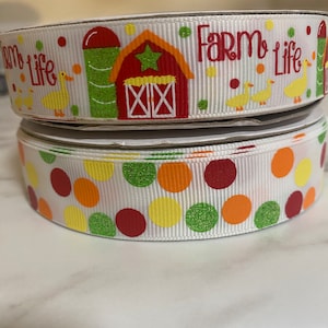 May include: Two rolls of white ribbon with a farm theme. The top roll has a red barn, silo, and ducks with the text "Farm Life". The bottom roll has a polka dot pattern with red, orange, yellow, and green dots.