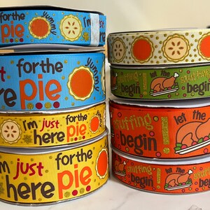 May include: A collection of eight colorful ribbon spools with Thanksgiving-themed designs. The ribbons feature phrases like "I'm just here for the pie", "Let the stuffing begin", and "Yummy".