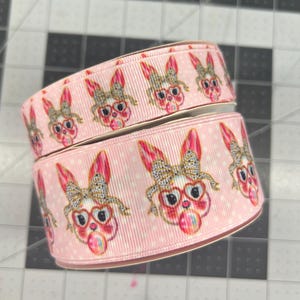 May include: Pink ribbon with a white polka dot pattern and a repeating design of bunnies wearing glasses and holding a pink lollipop.