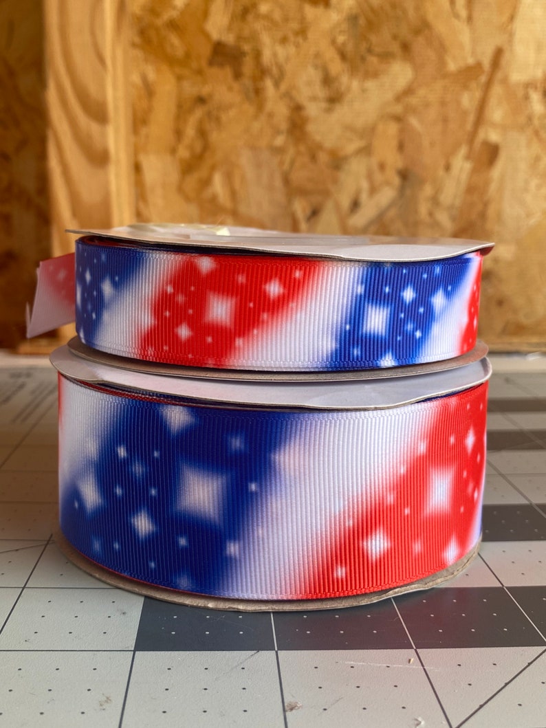 May include: Two spools of red, white, and blue ribbon with a star pattern. The ribbon is on a white background.