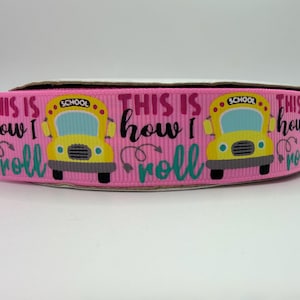 May include: A pink grosgrain ribbon featuring a repeating pattern of yellow school buses and the black and teal text "THIS IS how I roll". The ribbon is wound on a spool and displays a textured, ribbed surface throughout the entire length.